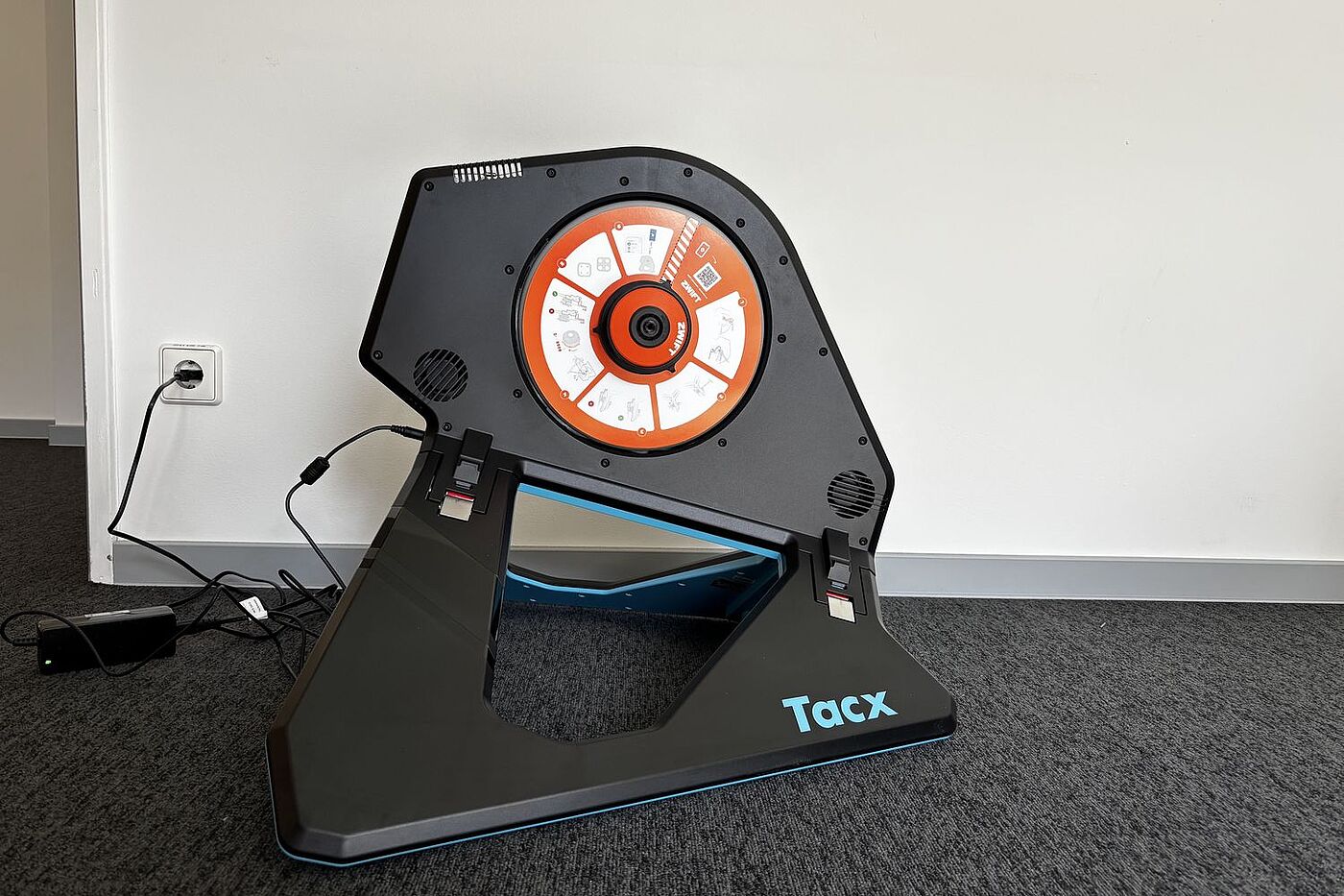 Der Smarttrainer Tacx Neo 2T steht auf grauem Teppich vor einer weißen Wand. 