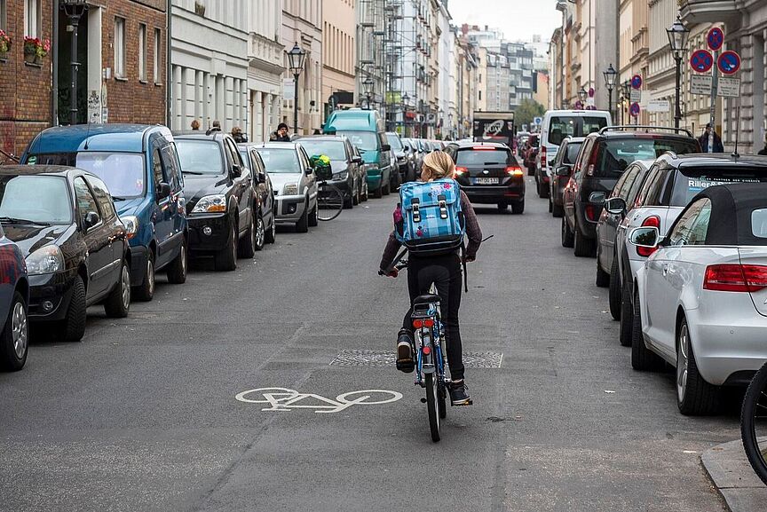 Gefahr durch Parken Mädchen auf dem Fahrrad fährt durch eine auf beiden Seiten zugeparkte Straße.